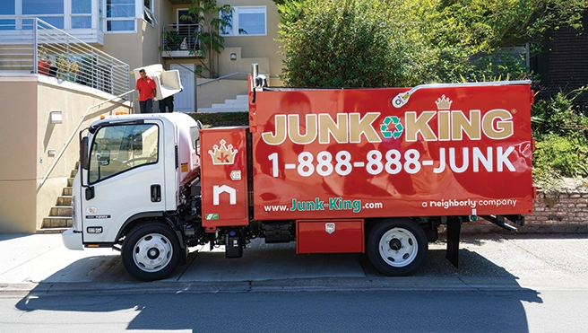 Red Junk King dump truck parked on the road beside a building.