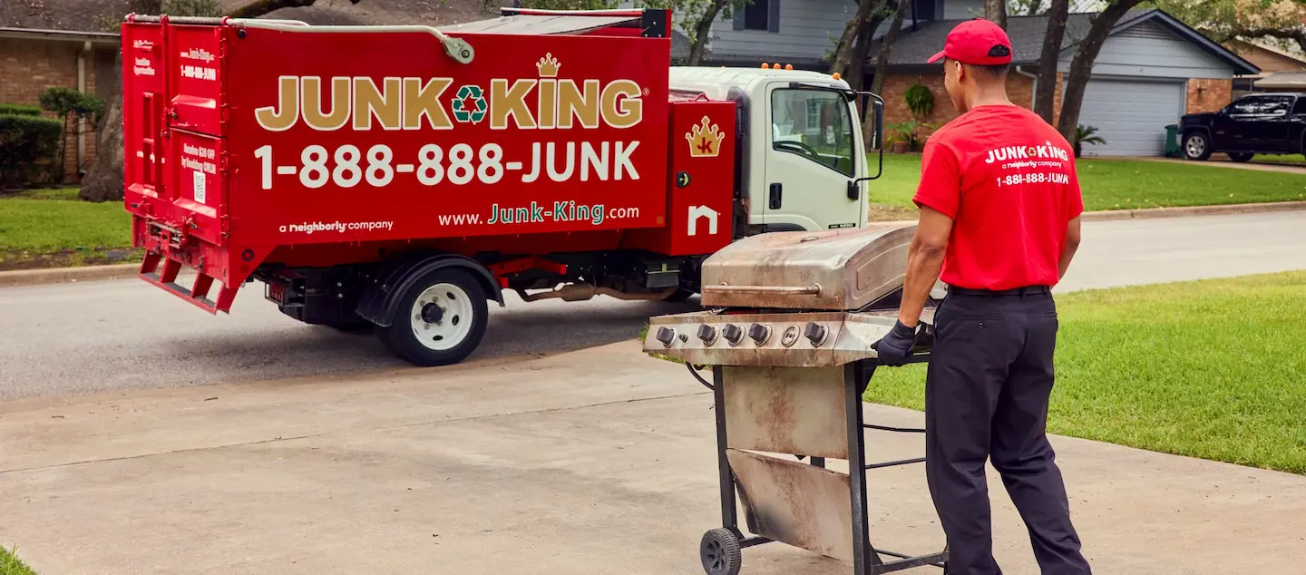 Junk King employee removing a barbecue grill from a residential driveway with a Junk King truck in the background.